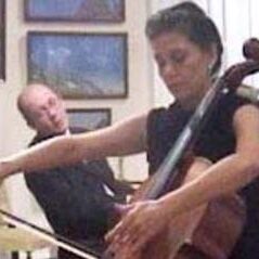 A man and woman playing the cello in front of paintings.